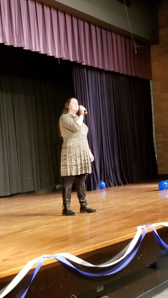 Young woman in beige skirt and sweater sings on a stage