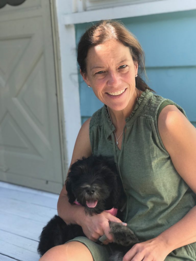 Dana Taylor is sitting on a step holding her dog 