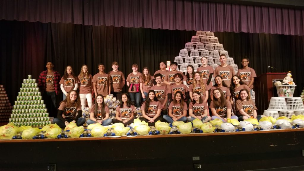 the full committee of students pose in front of a mountain of food that they collected 