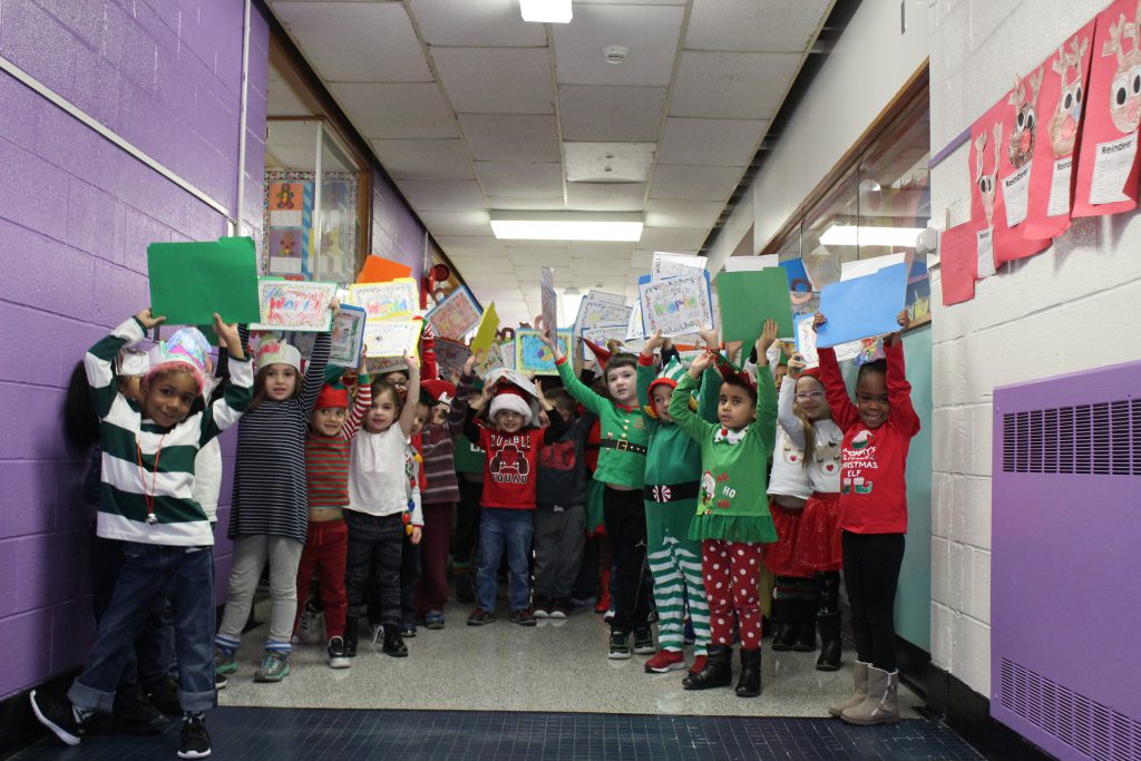 a group of kindergarten students are standing in the hallway holding up their artwork 