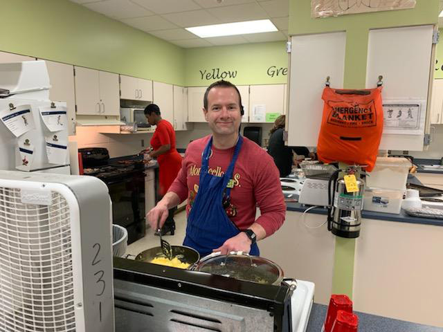 A man with a red shirt and blue apron makes scrambled eggs