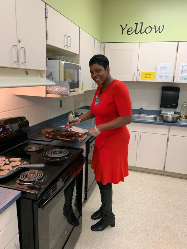 A woman in a red dress stands at a stove cooking sausage