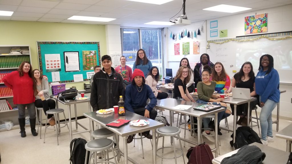 A group of 14 students and a teacher sit in a classroom.