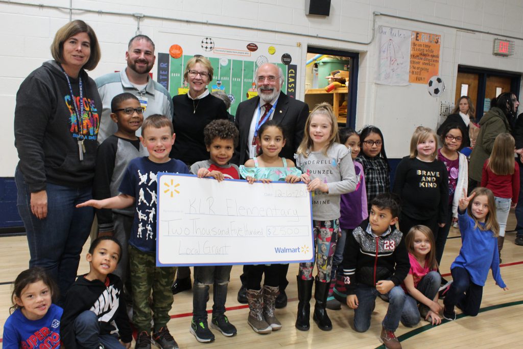 a group of students pose with representatives and hold a promotional check 