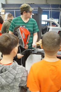 two young students are watching an older student weld