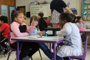 two students are seated at a table and engaged in a conversation 