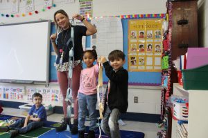 Ms Liebman is holding yesterday's paper chain and Brielle and Gabriel are holding a paper chain 