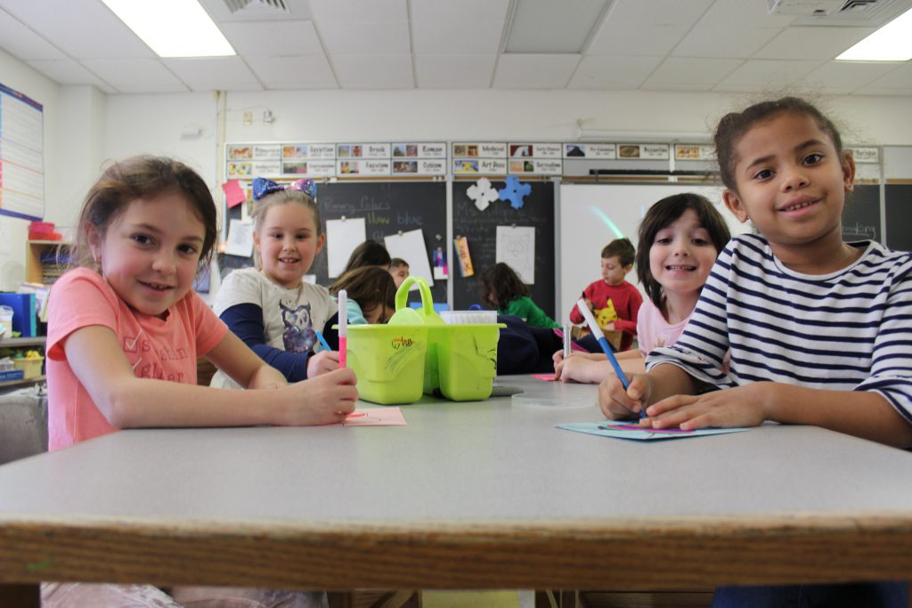 four students are sitting around a table and decorating cards 