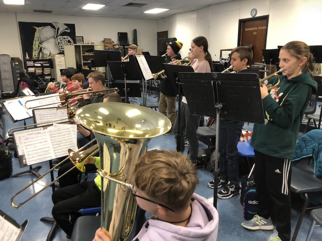 Ten students stand in two rows, all playing brass instruments