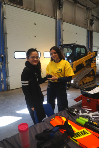 two students are standing near an excavator 