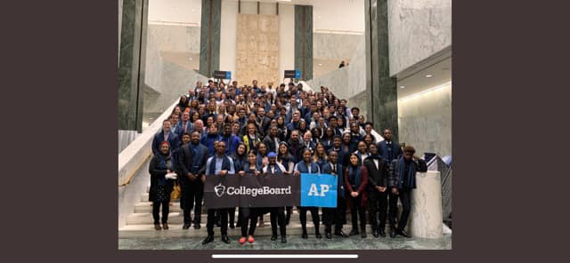 A very large group of high school students stand on the steps inside a building. Students in the front are holding signs that say College Board AP