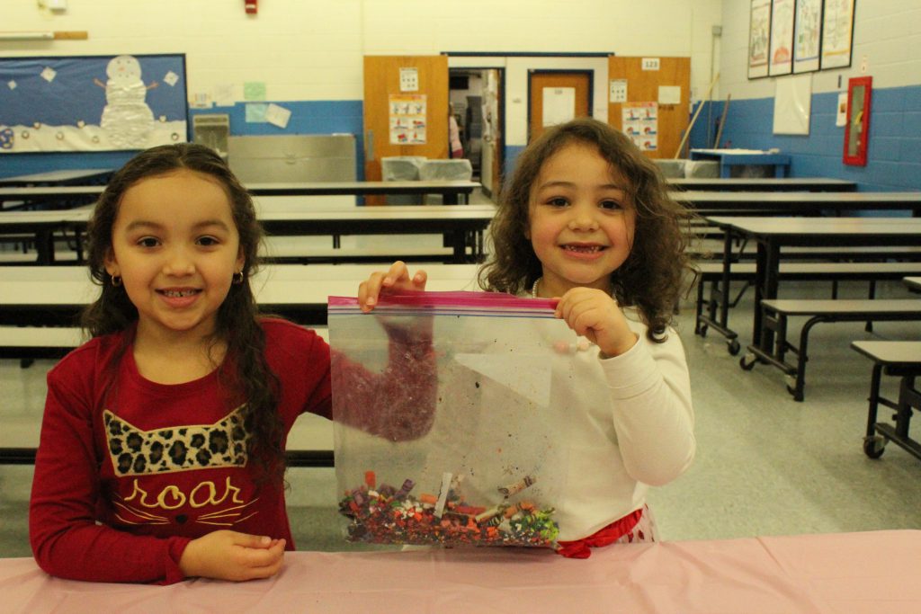 two students hold up a bag of crayon bits 