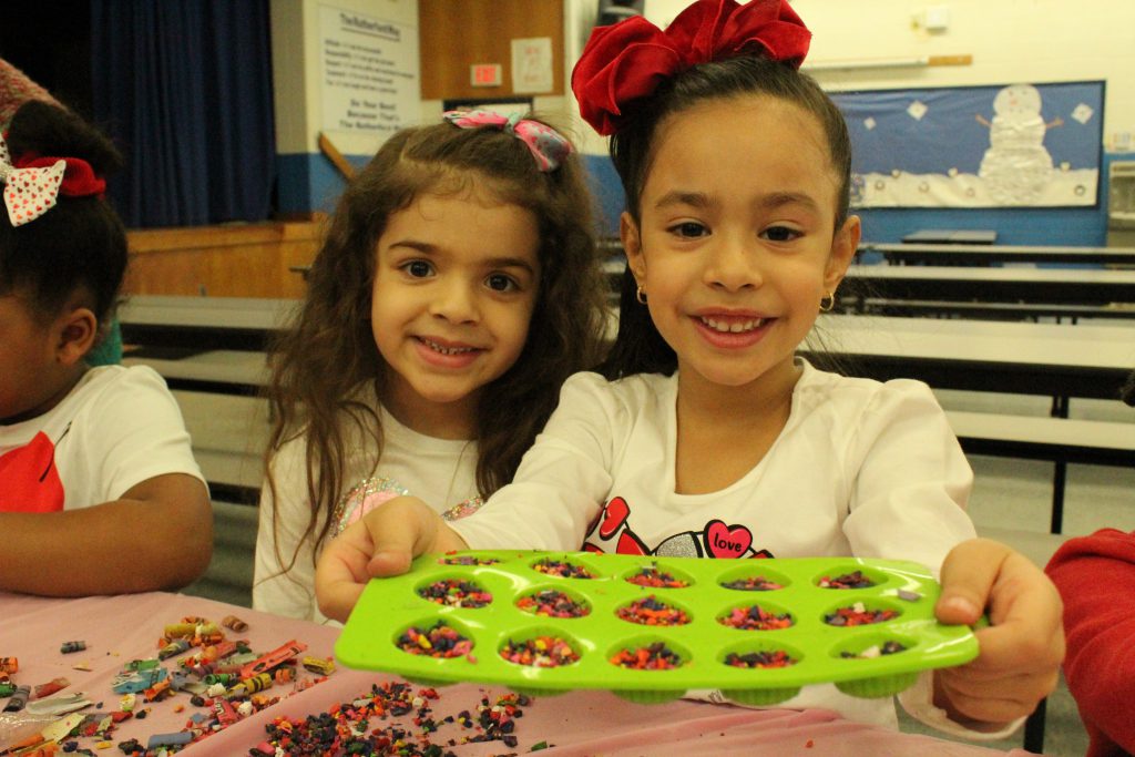 two students hold up a mold filled with crayon bits 