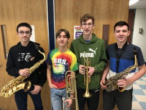 Four young men holding horns smile