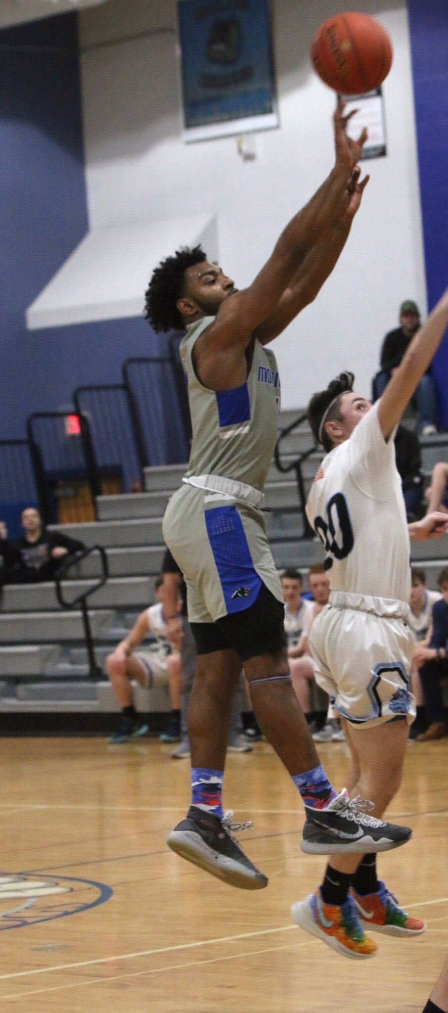 A basketball player wearing a gray and blue uniform goes up for a shot