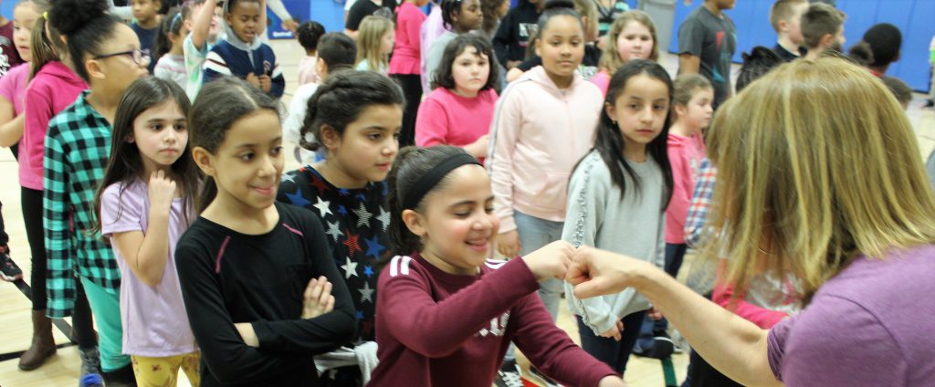 Many students stand in lines. A girl wearing a maroon shirt fist bumps