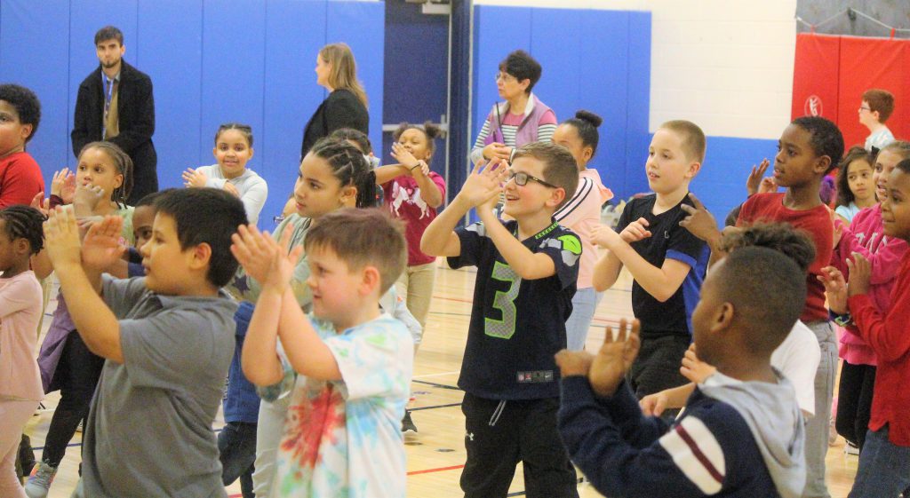 A large group of children standing and clapping their hands during an event.