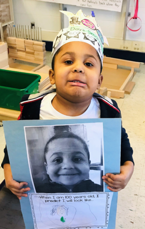 Armani Martinez is holding a piece of paper that has a photo of himself and a drawing of what he imagines he'll look like at 100 years of age. He is making a funny face. 