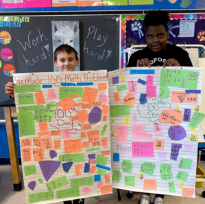 two fifth grade students are holding up a display of the math problems 