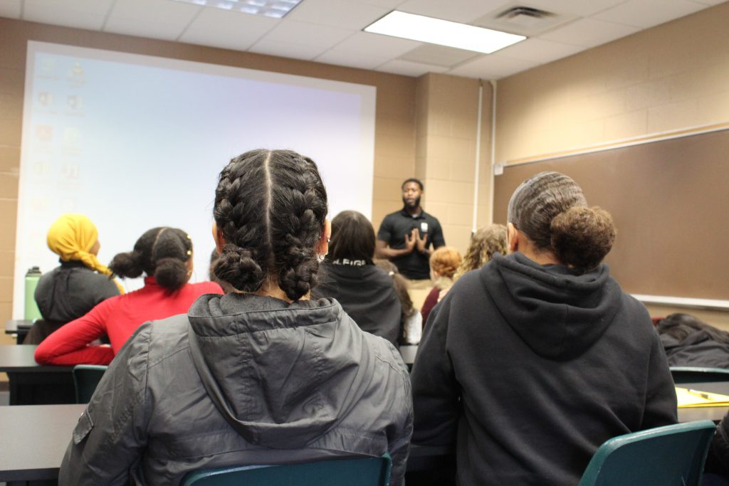 two students are seated in a class and listening to a teacher 