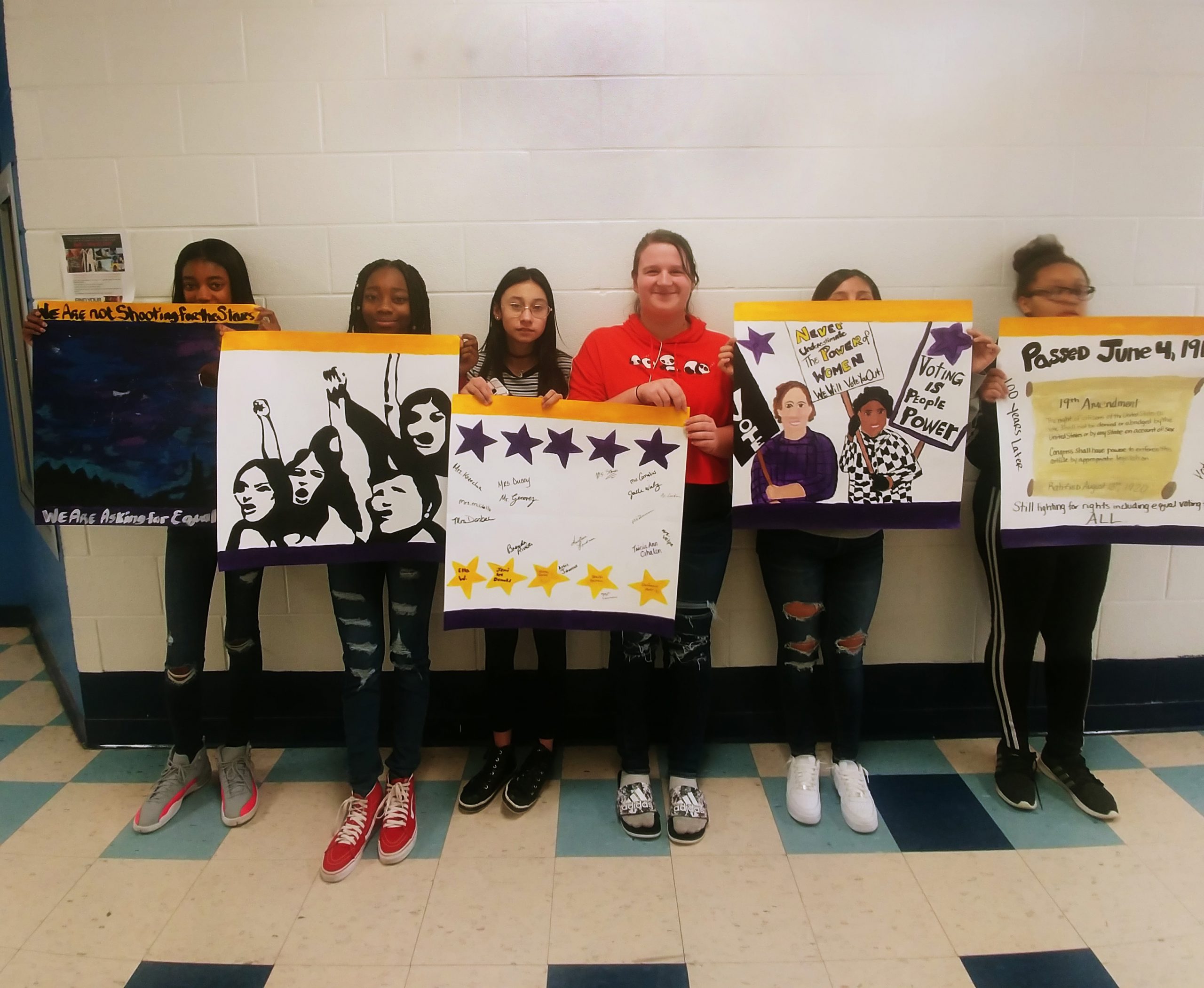 Six middle school aged girls hold up their posters made to commemorate the 100th anniversary of the 19th amendment