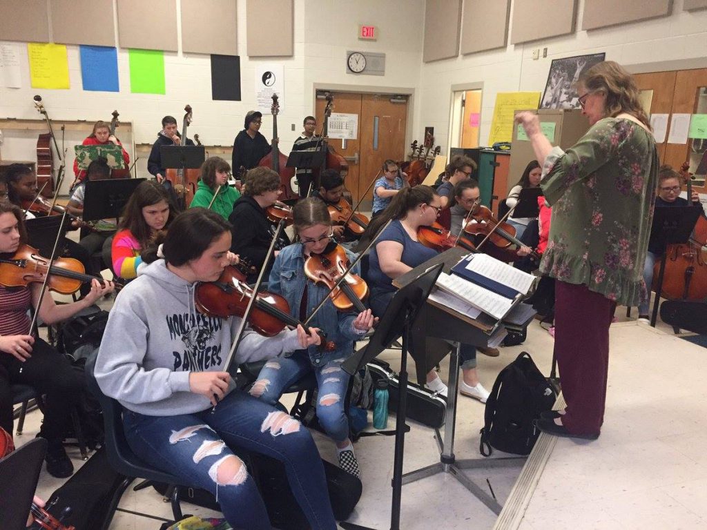 Nancy Wegrzyn is standing in the middle of students playing instruments and conducting 