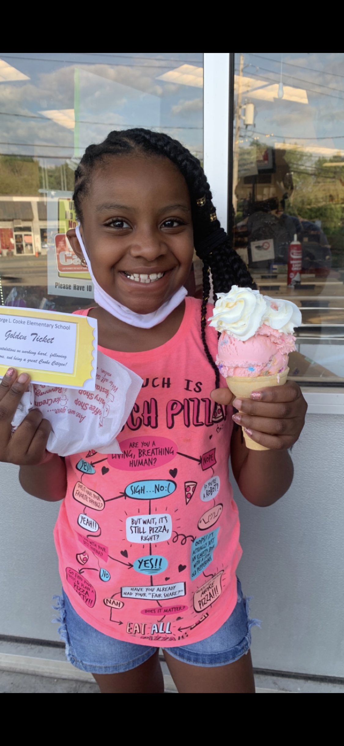 Laday, wearing a pink shirt is holding up an ice cream cone and smiling.