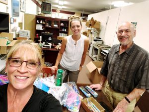 A man and two women smile as they put together packages of arts supplies