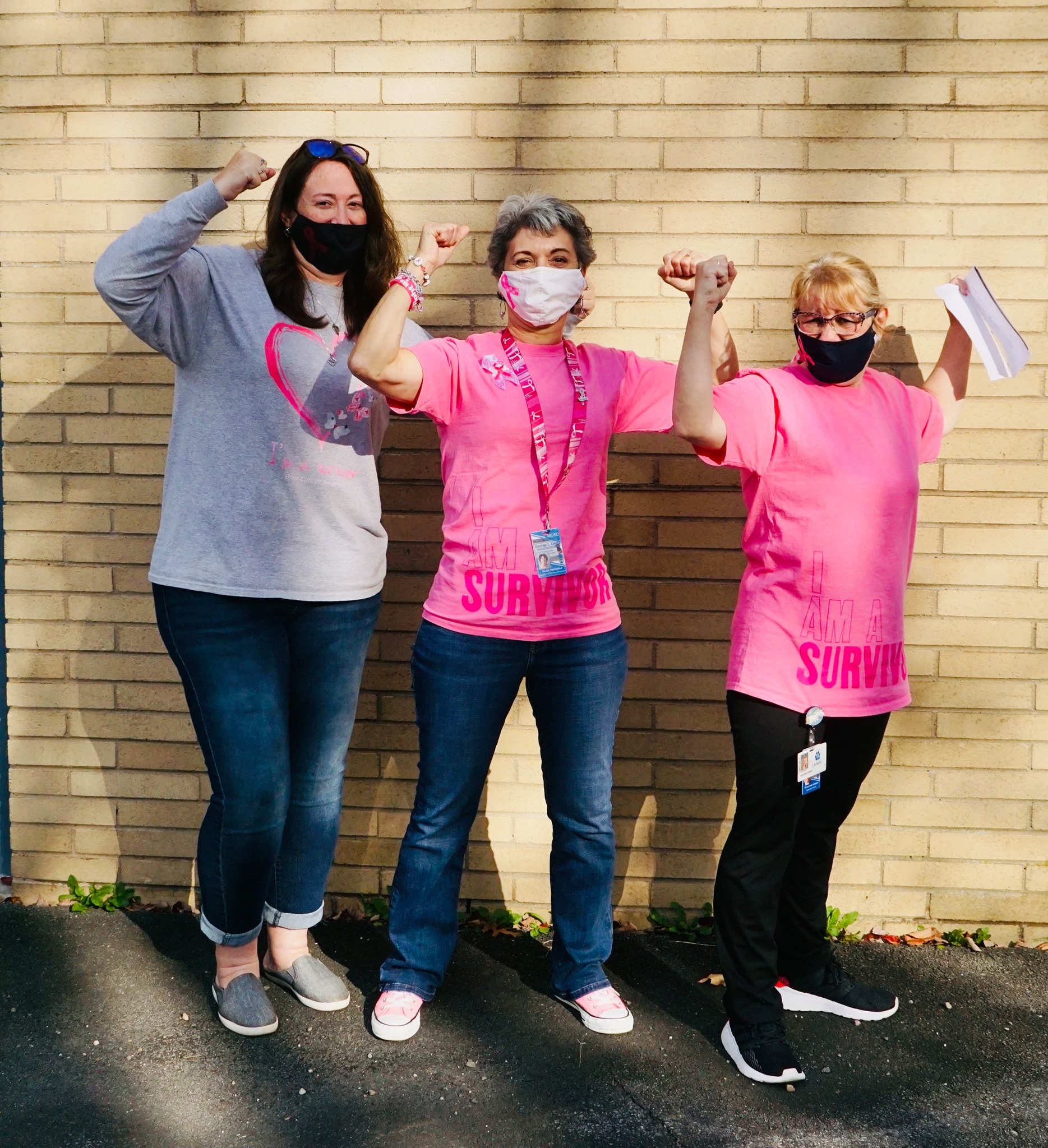 three women wearing pink and denim have their arms raised triumphantly in the air