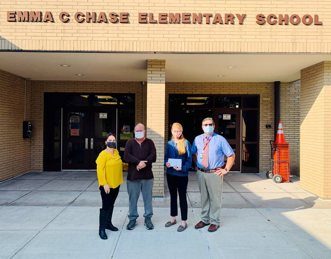 Four people out in front of a tan brick building wiht the words Emma C Chase Elementary School