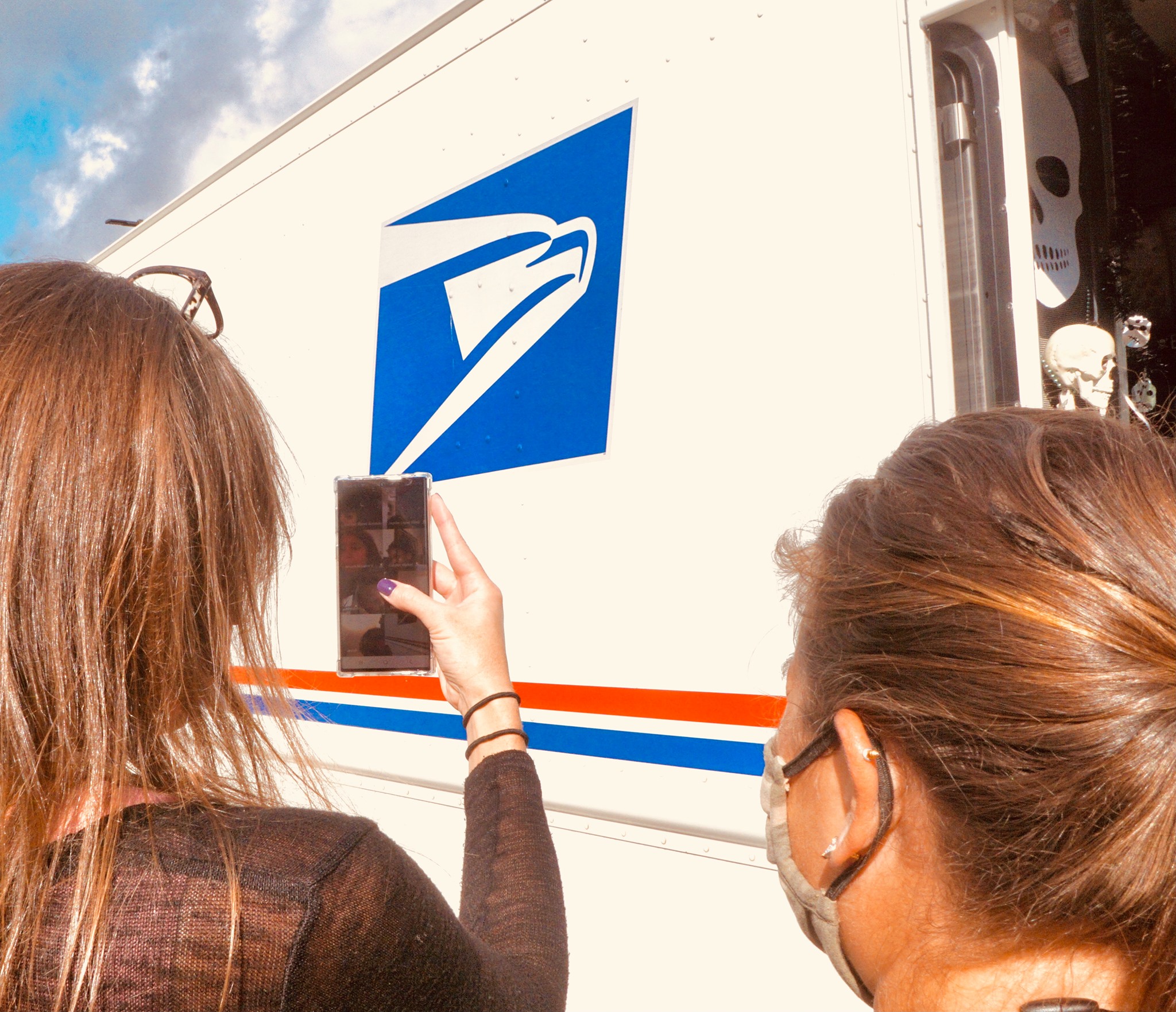 two teachers are standing in front of a mail truck and filming