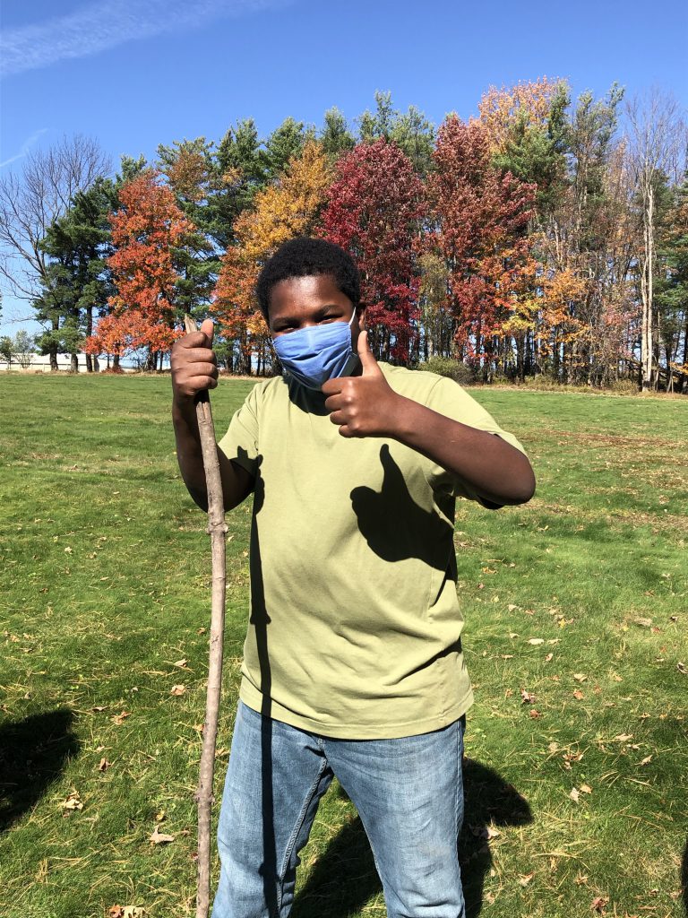 a child in a yellow shirt is holding a hiking stick outdoor and giving a thumbs up sign