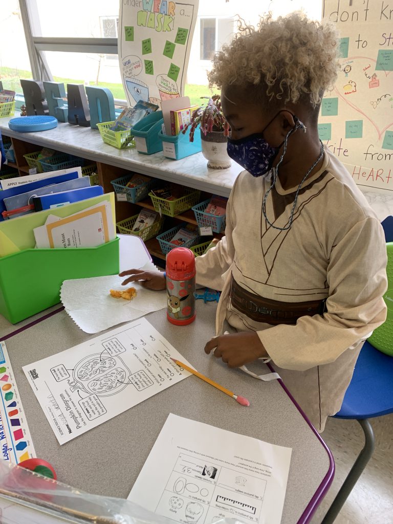 a student is standing up at a desk looking down and pumpkin seeds and pulp 