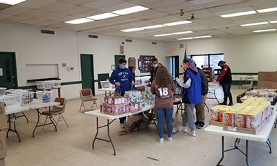 A group of high school students are around a table that is filled with canned goods.