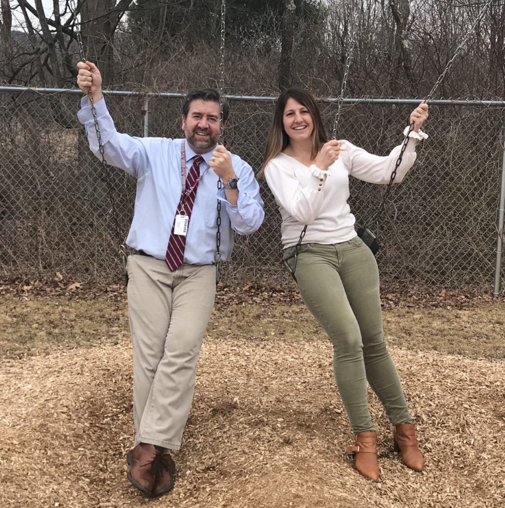 Ginny Gallet and Bill Frandino are sitting on swings and smiling 