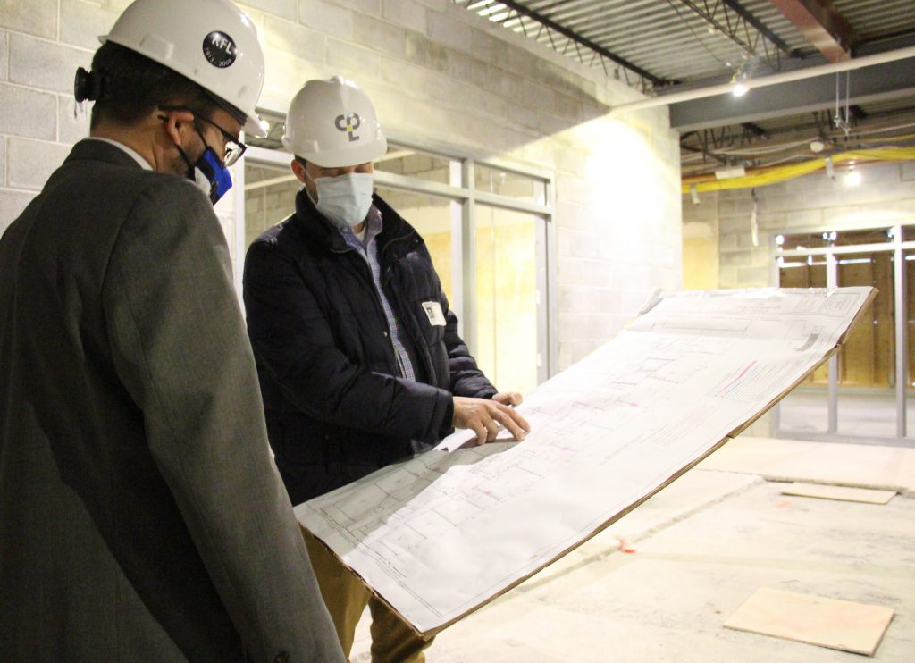 Two men in hard hats look at architectural plans 