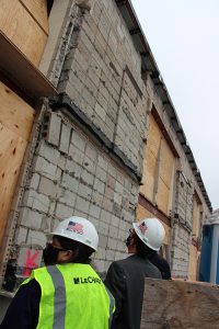 Two people in hard hats look up at a wall built from cinderblocks