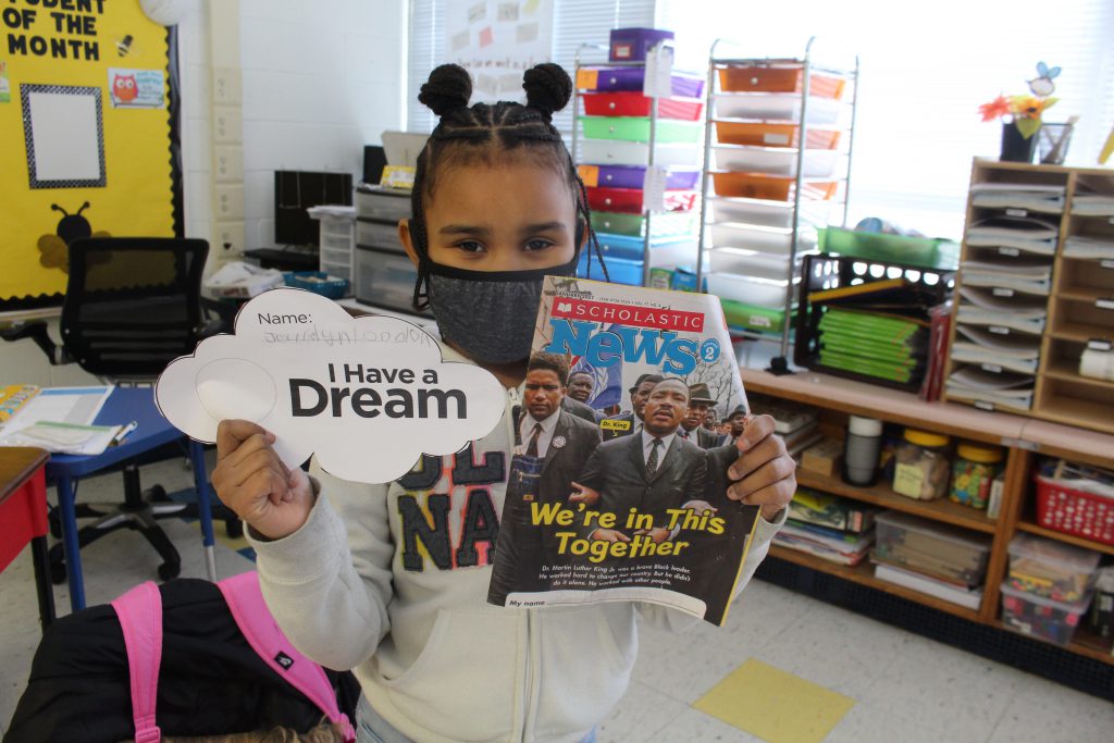 a young girl holds up the craft she made and a photo of Dr. Martin Luther King, Jr. 