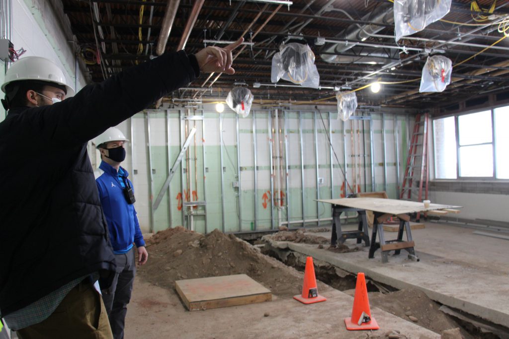 Two men look at the construction being done in one of the science labs. Two orange cones mark where a trench has been dug.