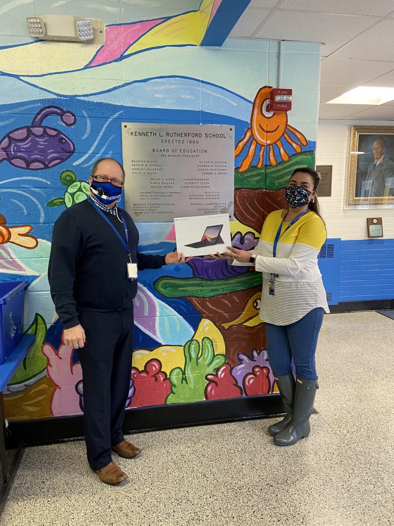 Mr. Palmer and Ms. Kreeger are standing in a hallway holding the new tablet and smiling 