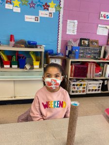 a young girl is sitting at a desk holding a rain stick