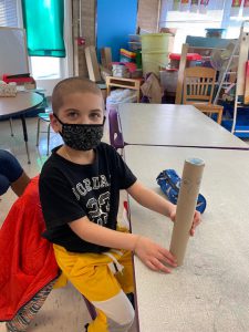 a young boy is sitting at a desk and holding a rain stick