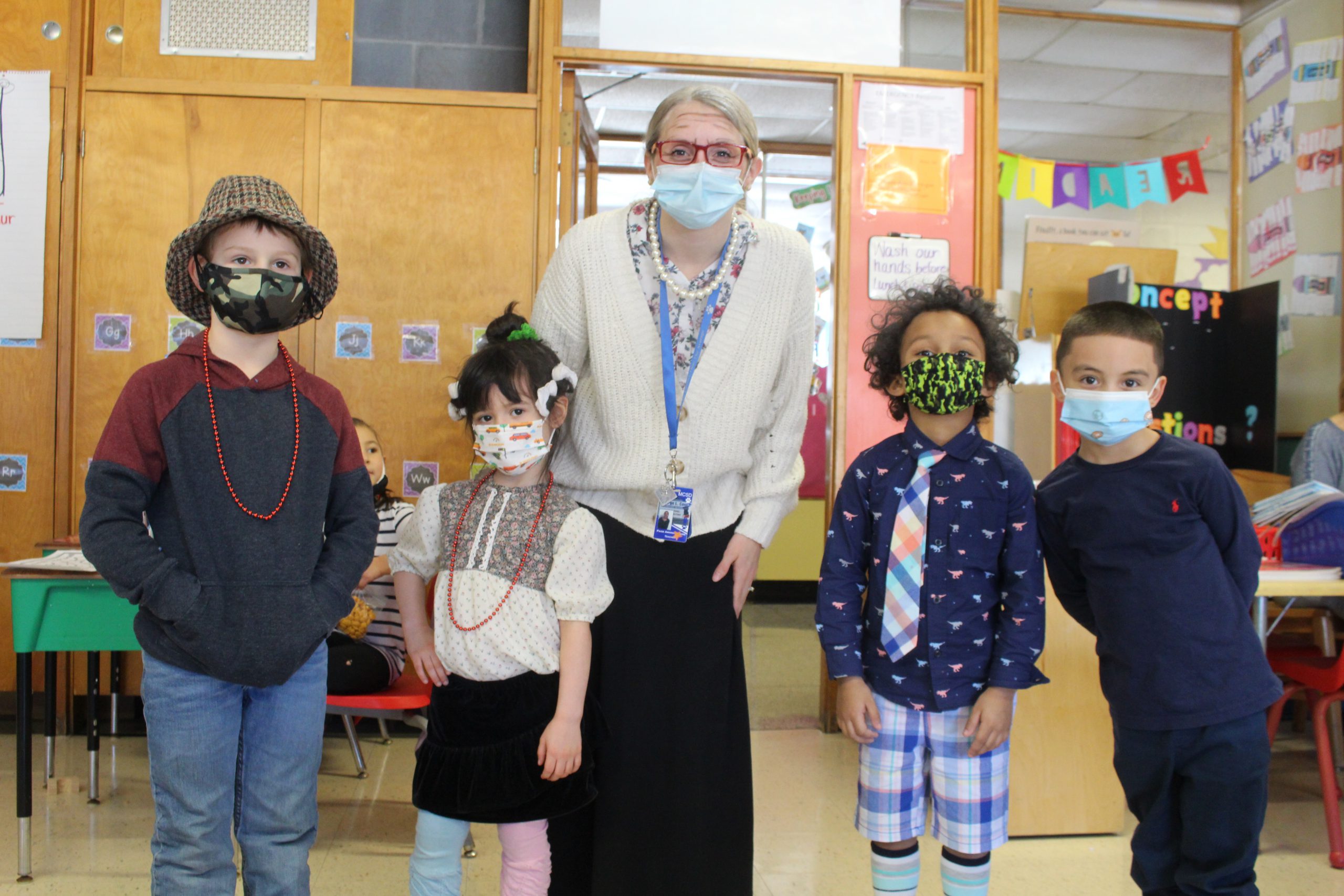 a teacher and students, all wearing centenarian costumes, are posting together and smiling