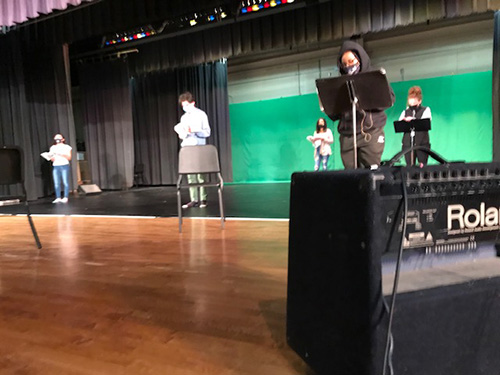 high school students on a stage, separated, with a green background