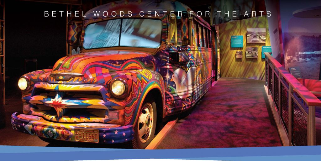 bus painted all different psychedelic colors in a room with pink lighting. SaysBethel Woods Center for the Arts across the top