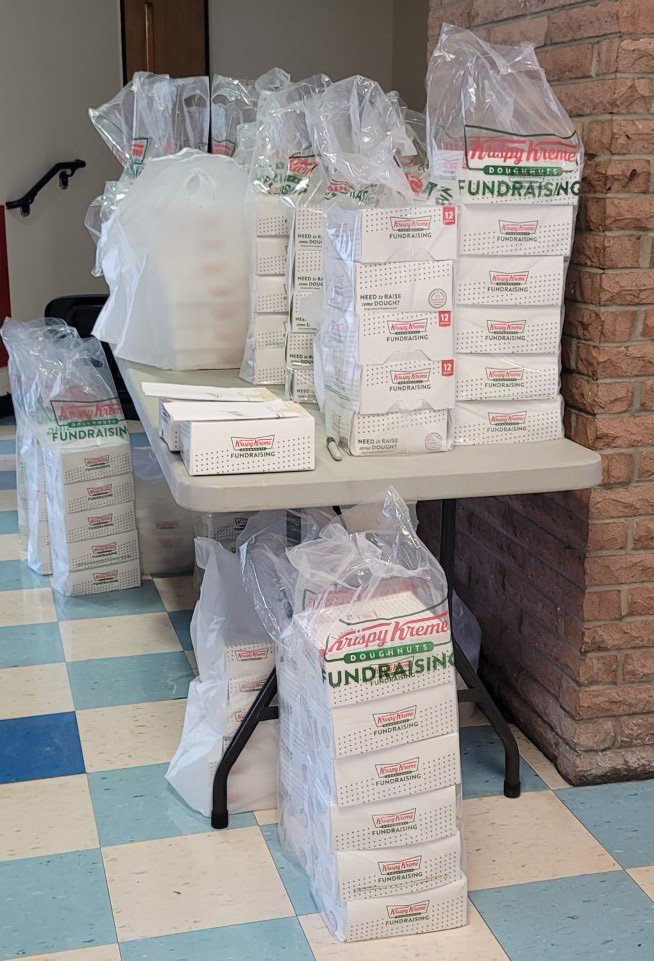 A table with numerous piles of white boxes on top and on the floor in bags. 