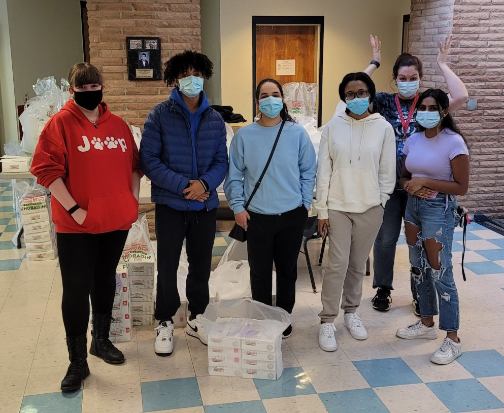 A group of six students standing in a room. All ae wearing masks. 