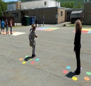 Two students standing on blacktop. At each of their feet is a circle of different colored dots - blue, red, yellow, orange, green