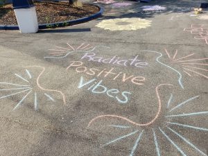 Chalk on the blacktop that says Radiate Positive Vibes in different pastel colors