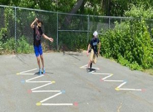 A zig zap drawn on blacktop with two older students weaving their way through it.